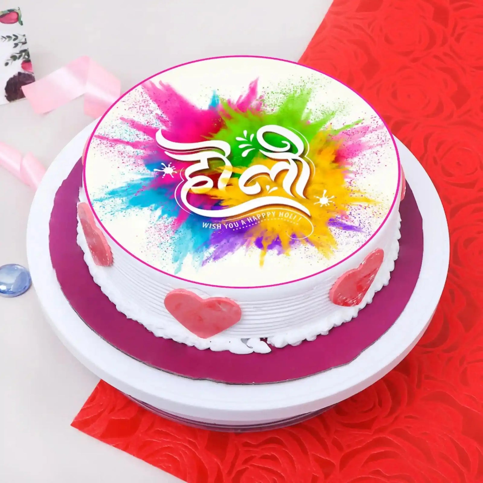 Decorated Holi Festive Cake with white frosting, pink heart accents, colorful splash design, for celebrations